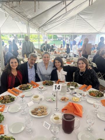 Senator Wahab smiles at the camera with her honorees as they sit around a dining table under a tent.